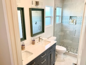 A bathroom with a double sink, a toilet, a glass shower enclosure, and a vanity with drawers.