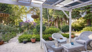 Relax in a serene outdoor space with a covered pergola, wicker chairs, and lush greenery.