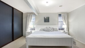 Un dormitorio con una cama grande, dos mesitas de noche con lámparas, un cabecero y una ventana con cortinas.