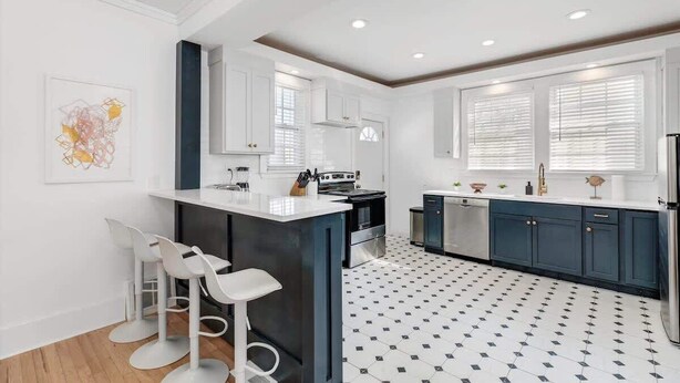 A modern kitchen with white cabinetry, a central island with bar stools, and a patterned floor. - Sleeps 14! 10 Mins to Downtown + Driveway Parking (Detroit)