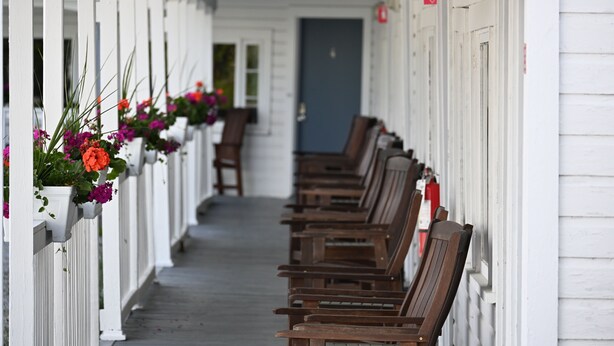 Eine Reihe aus Holzbanken entlang einer weißen Veranda mit Blumenkästen auf der linken Seite.