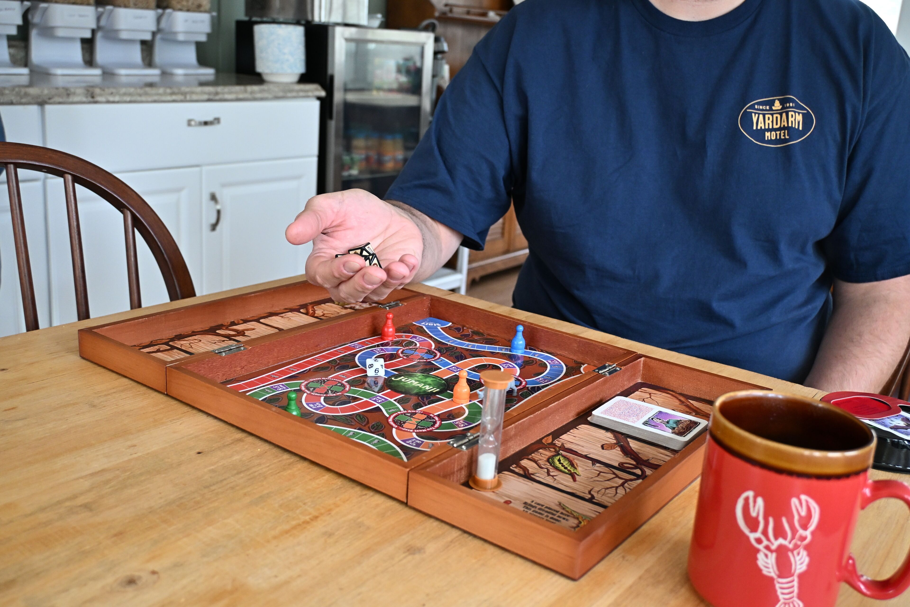 Iemand speelt een bordspel op een houten tafel, met een rode mok en een dienblad met spelstukken.
