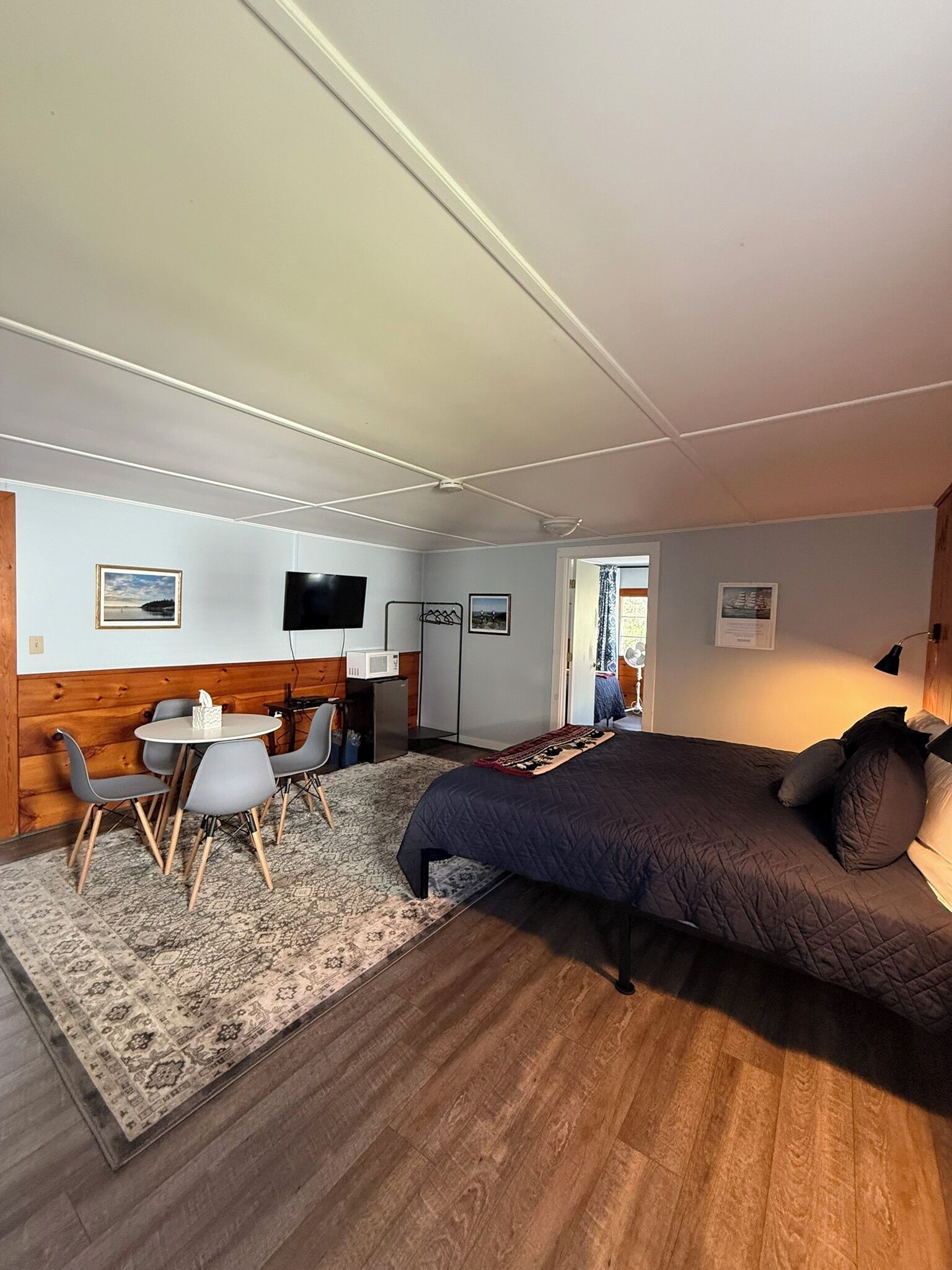 Un dormitorio con cama, escritorio, sillas, televisor y ventana.