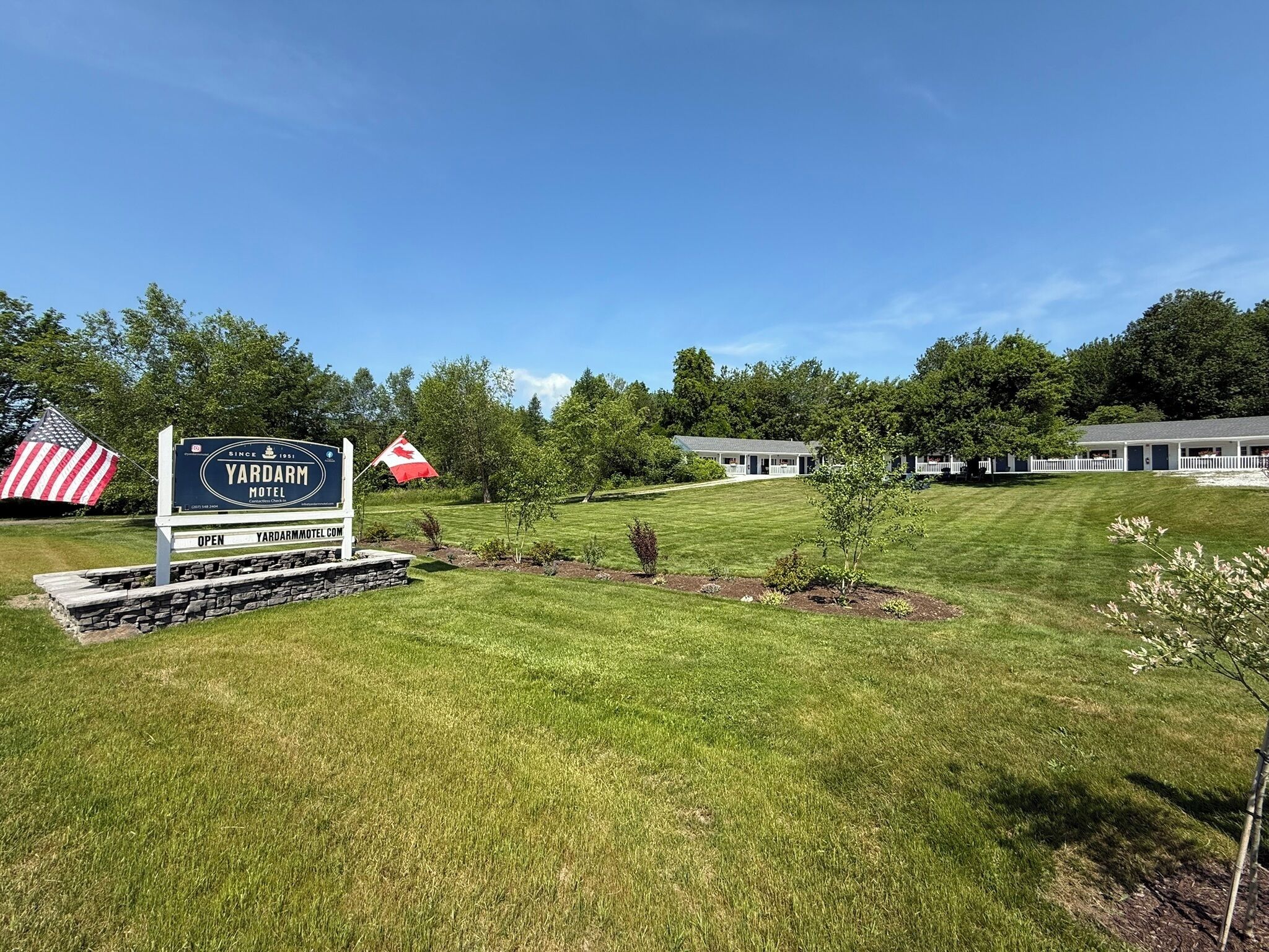 A sign for Yardarm Motel with a flag, a well-maintained lawn, and a row of motel buildings.