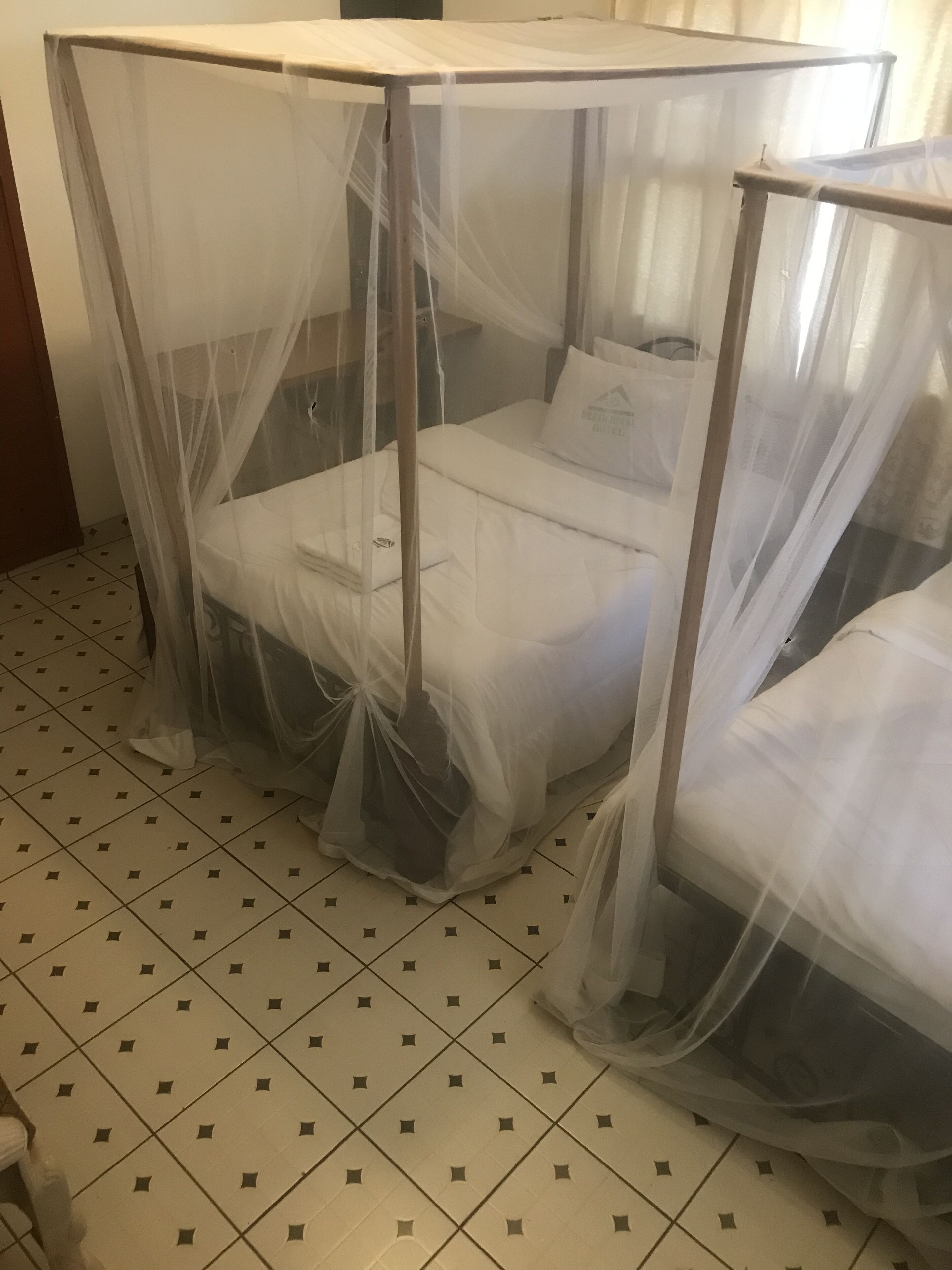 Ein Zimmer mit einem Bett, das mit einem Moskitonetz verhängt ist, einem Fliesenboden und einer schlichten Wand.