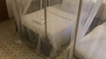 Ein Zimmer mit einem Bett, das mit einem Moskitonetz verhängt ist, einem Fliesenboden und einer schlichten Wand.