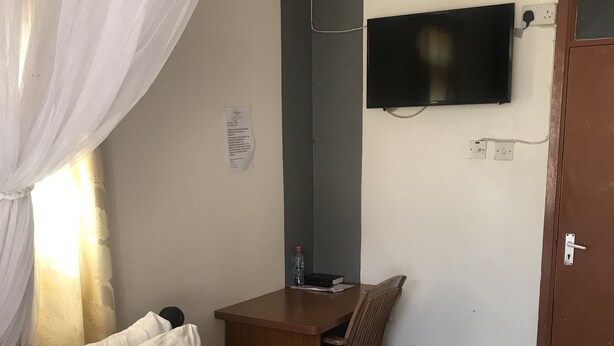 Et hotelværelse med en seng, et skrivebord, en stol, et fjernsyn ophængt på væggen og en dør.