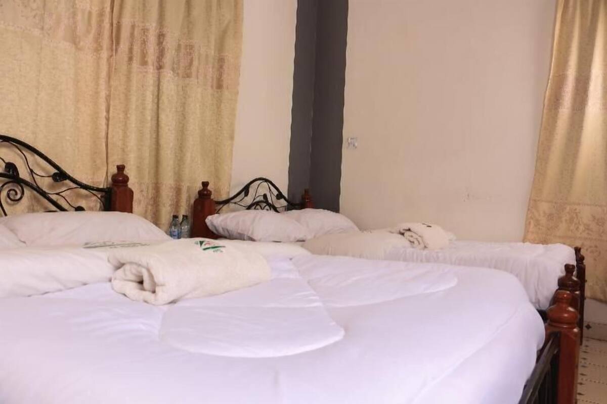 Una habitación de hotel con dos camas individuales, un ventanal con cortinas y una pared lisa.