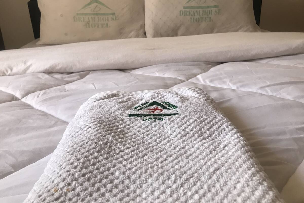 Una cama bien hecha con un edredón blanco y almohadas, cada una con el logotipo del Dream House Hotel.