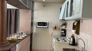 A compact kitchen with a microwave, gas stove, and a sink. - El Nogal, Acogedora Cabaña con Jardín y Cochera (Vistalba Luján de Cuyo)