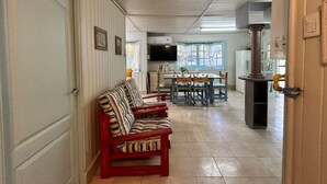 A corridor with a sofa, a dining area with a table and chairs, and a kitchen area with a stove and sink. - El Nogal, Acogedora Cabaña con Jardín y Cochera (Vistalba Luján de Cuyo)