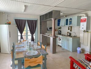Een compacte keuken met een centraal eiland, een eethoek met een tafel voor vier personen, en een rode stoel.