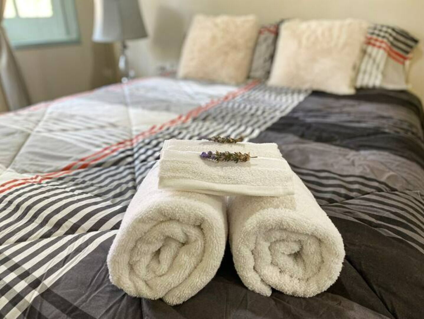 Una cama bien hecha con una colcha a rayas, dos toallas blancas enrolladas y un pequeño objeto decorativo sobre la cama.