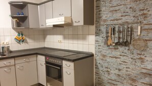 Une cuisine équipée d’une cuisinière, d’un four et de placards. On y trouve une étagère avec des ustensiles de cuisine et une serviette accrochée au mur.
