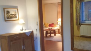Une pièce avec un bureau en bois, une lampe, un tableau encadré au mur et une fenêtre avec des rideaux.