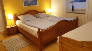 Un lit bien fait, avec une tête de lit en bois, deux lampes de chevet, un tableau au mur et une fenêtre donnant sur des arbres.