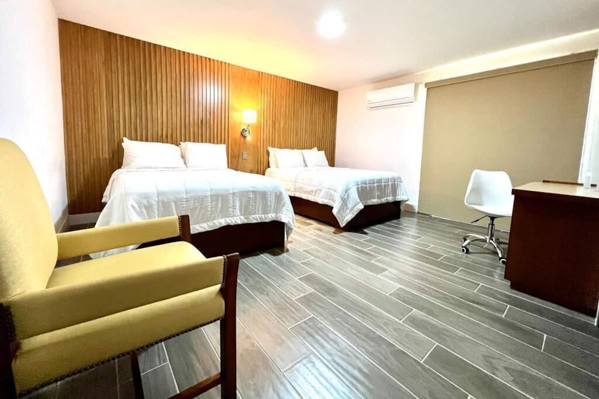 A hotel room with two beds, a desk, a chair, and a wooden accent wall.