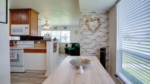 A kitchen with wooden cabinets, a microwave, and a stove. There is a heart-shaped decoration on the brick wall and a window with blinds. - Charming & Cozy: Close to Beach & Shops ~ Parking! (Port Charlotte)