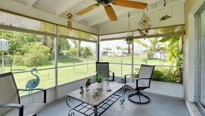 A covered patio with a ceiling fan, a table with chairs, and a view of a fenced yard with greenery. - Charming & Cozy: Close to Beach & Shops ~ Parking! (Port Charlotte)