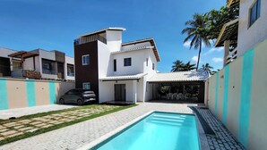 A modern house with a swimming pool, a car parked outside, and a patio area.