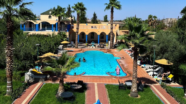 A swimming pool surrounded by palm trees and a building with arches. - Hotel Riad Qodwa  (Marrakesh)