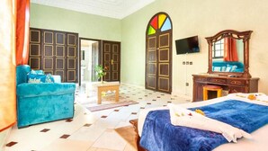 A hotel room with a large bed, a sofa, a desk, and a TV. - Hotel Riad Qodwa  (Marrakesh)
