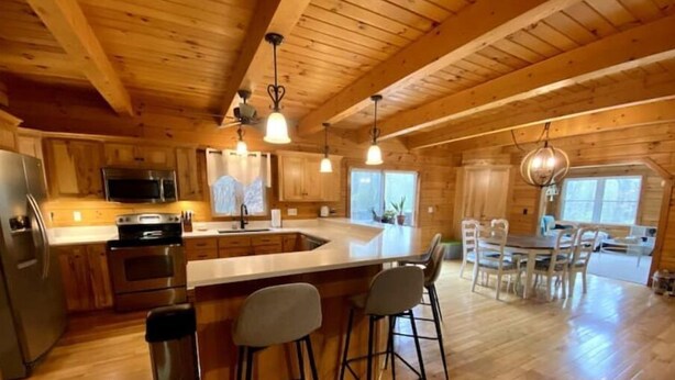 Interior de una cabaña de madera con cocina, comedor y taburetes de bar.