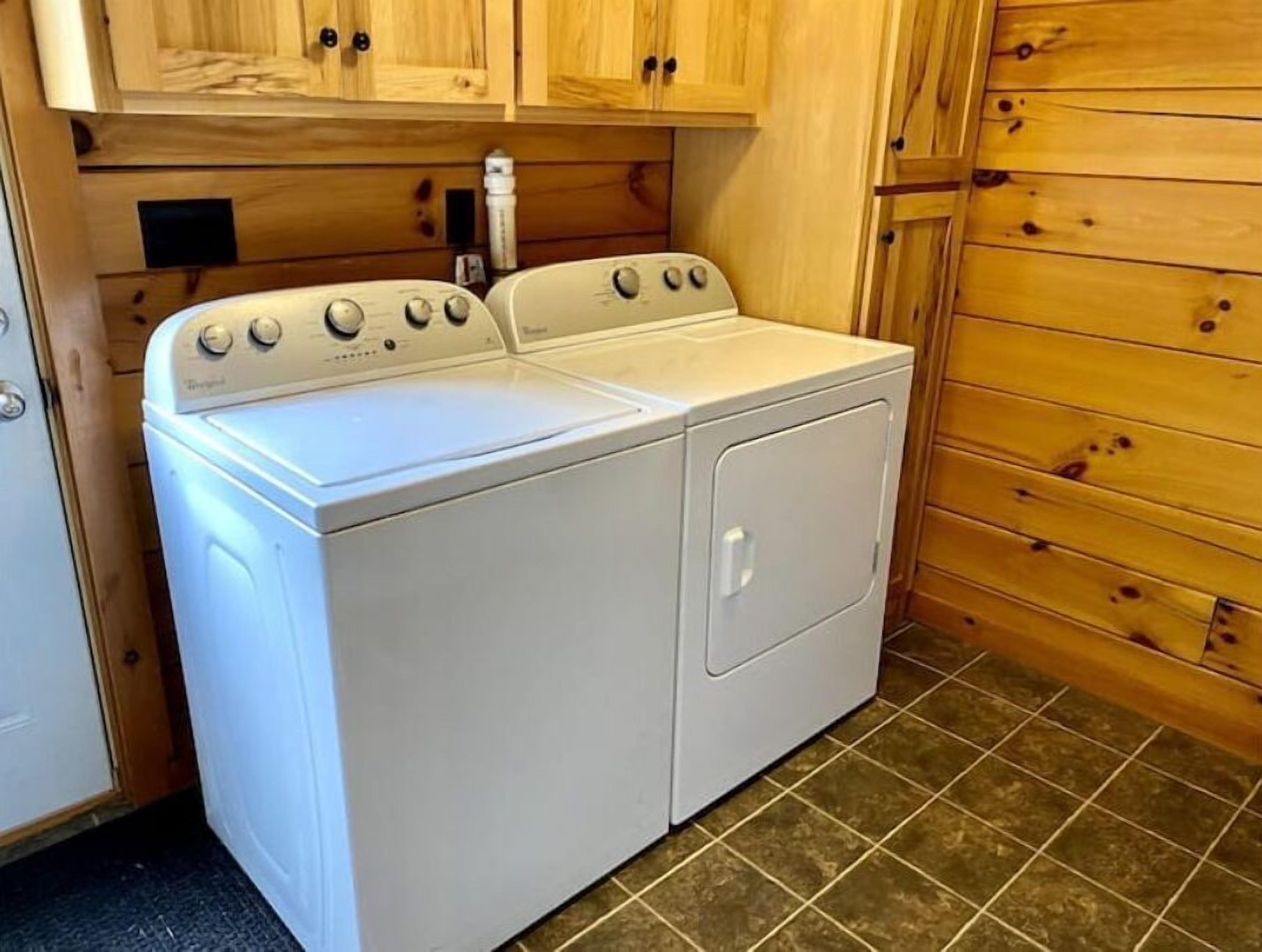 A compact laundry room with a front-loading washer and dryer, wooden cabinets, and a tiled floor.