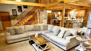 Una sala de estar moderna con un sofá seccional, una mesa de centro de madera y una escalera que lleva a un nivel superior.
