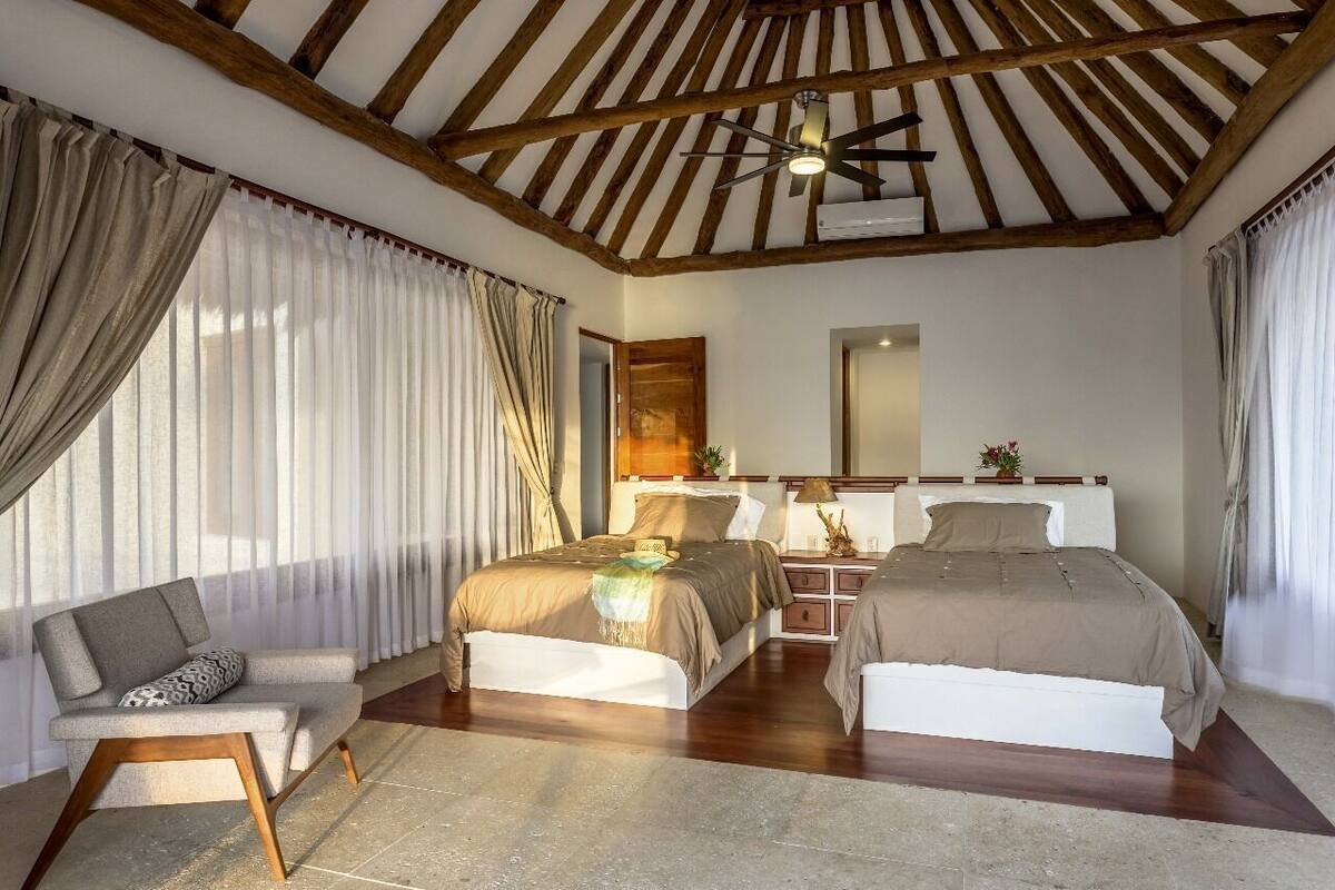 A bedroom with a wooden ceiling, a bed, a chair, a nightstand, and a mirror.