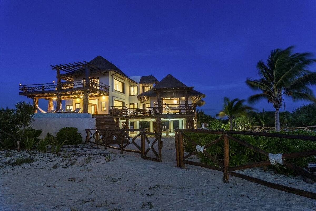 A beachfront property with a large house, a covered patio, and a sandy beach area.