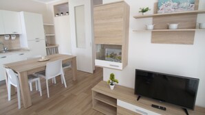 Een moderne keuken met witte kasten, een houten eettafel en stoelen. Er staat een televisie op een houten dressoir en een kleine plant op de tafel.