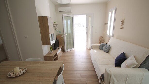 Een moderne woonkamer met een houten eettafel, een witte bank met kussens en een schuifpui die leidt naar een balkon.
