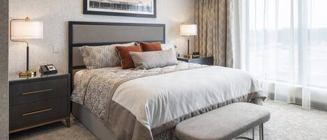 A hotel room with a large bed, two bedside tables with lamps, a bench, and a large window with curtains.