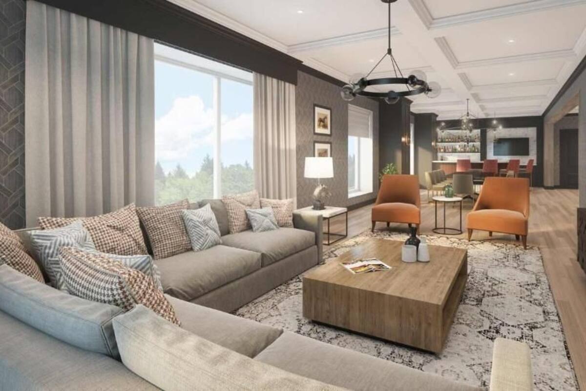 A modern living room with a sofa, coffee table, and chairs. There is a TV mounted on the wall and a dining area in the background.