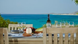 A table set for a meal with a bottle of wine, glasses, and a variety of food items, overlooking a coastal view. - Villa 'Azure' a seaside diamond in  Villa Paradise Boutique Hotel (Naxos)