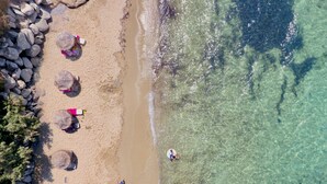A beach with clear water, rocks, and several thatched-roof huts. - Villa 'Azure' a seaside diamond in  Villa Paradise Boutique Hotel (Naxos)