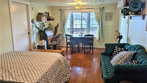 Una habitación acogedora con cama, sofá verde, mesa de comedor con sillas y ventana con cortinas.