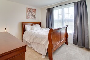 Un dormitorio con cama de madera, una mesita de noche, una lámpara de pared y un ventanal con cortinas.