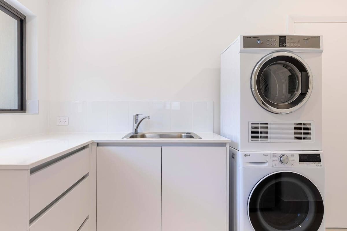 A laundry room with stacked washers and dryers, a sink, and cabinets.