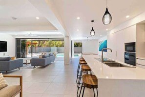 A modern kitchen with a bar area, a dining space with sofas, and a large window.