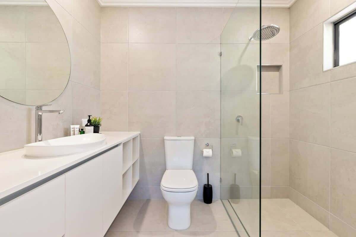 Un baño moderno con cabina de ducha de vidrio, inodoro blanco y un espejo grande.