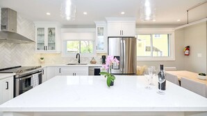 Une cuisine moderne dotée d’un grand îlot central, d’appareils électroménagers en acier inoxydable et de luminaires suspendus.