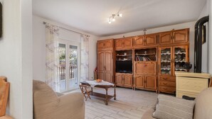 A living room with a sofa, a dining table with a bowl of fruit, wooden cabinets, and a television. - Nice apartment in Sveti Juraj with house sea view (Sveti Juraj)