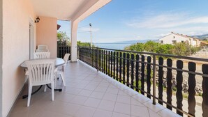 A balcony with a table and chairs, a view of the sea, and a building in the background. - Nice apartment in Sveti Juraj with house sea view (Sveti Juraj)