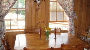 A wooden dining table with chairs, a vase with flowers, and a candle on the table. - Welcome to Valhalla (Rangeley)