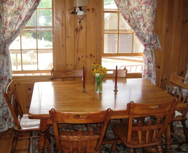 A wooden dining table with chairs, a vase with flowers, and a candle on the table. - Welcome to Valhalla (Rangeley)