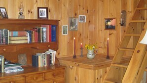 A wooden interior with a bookshelf, framed photos, a vase with flowers, candles, and a wooden ladder. - Welcome to Valhalla (Rangeley)