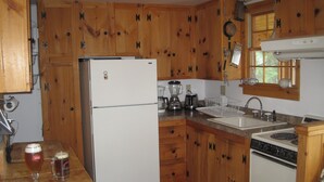 A kitchen with wooden cabinets, a refrigerator, a sink, a stove, and a coffee maker. - Welcome to Valhalla (Rangeley)