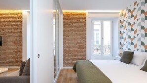Een moderne slaapkamer met een bakstenen muur, een groot bed, een groene plaid en een balkon met een patroonmuur.